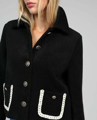 Femme portant une veste en laine noire avec des boutons en cresta argentée et deux poches avant soulignées d'un passepoil blanc.
