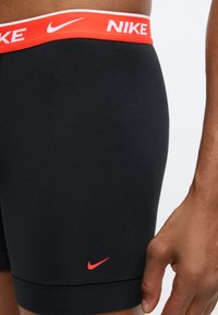 Fekete nylon boxeralsó piros Nike derékpánttal és kis piros logóval az alsó bal oldalon. Sima textúra. Testhez simuló kialakítás.
