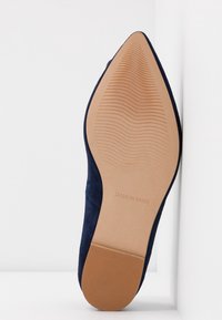 Semelle d'une chaussure plate bleu marine à bout pointu, face inférieure visible, motif de grip texturé, tampon "Made in Spain" visible près de la voûte plantaire.
