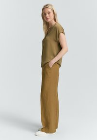 Blouse à manches courtes vert olive associée à un pantalon taille haute à jambe large jaune moutarde et des baskets blanches. Texture lisse, coupe décontractée.