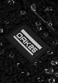 Fekete, textúrált szövet, fényes cseppekkel és egy fekete, téglalap alakú címkével, amelyen fehér, dombornyomott felirat olvasható: "OAK25".