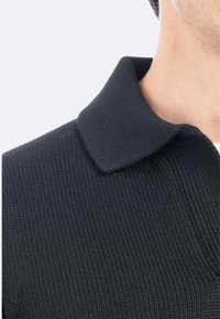 Polo shirt nero in maglia con colletto strutturato. Il tessuto ha una superficie texturizzata che evidenzia un motivo a coste.