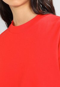 Camiseta roja de algodón con cuello redondo y mangas cortas, textura lisa con un color sólido y sin patrones o acentos visibles.