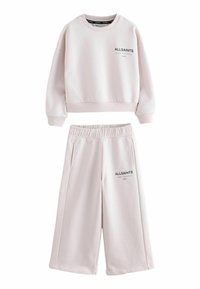 Różowa, krótka bluza i szerokie spodnie z logo "ALLSAINTS" oraz japońskimi znakami na klatce piersiowej i udzie.