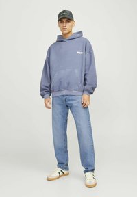 Hellblauer Hoodie mit Kängurutasche, kombiniert mit hellblauen geraden Jeans und weißen Sneakern mit grünen Akzenten. Schwarze Kappe.