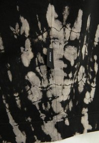 Černá a béžová batikovaná látka s vertikálním švem a malou černou etiketou s nápisem "CHASIN'".