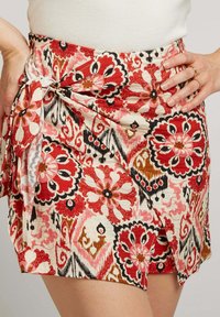 Jupe mini à motifs floraux avec des motifs rouges, roses et noirs sur fond clair, avec un nœud sur le côté et des bords festonnés.