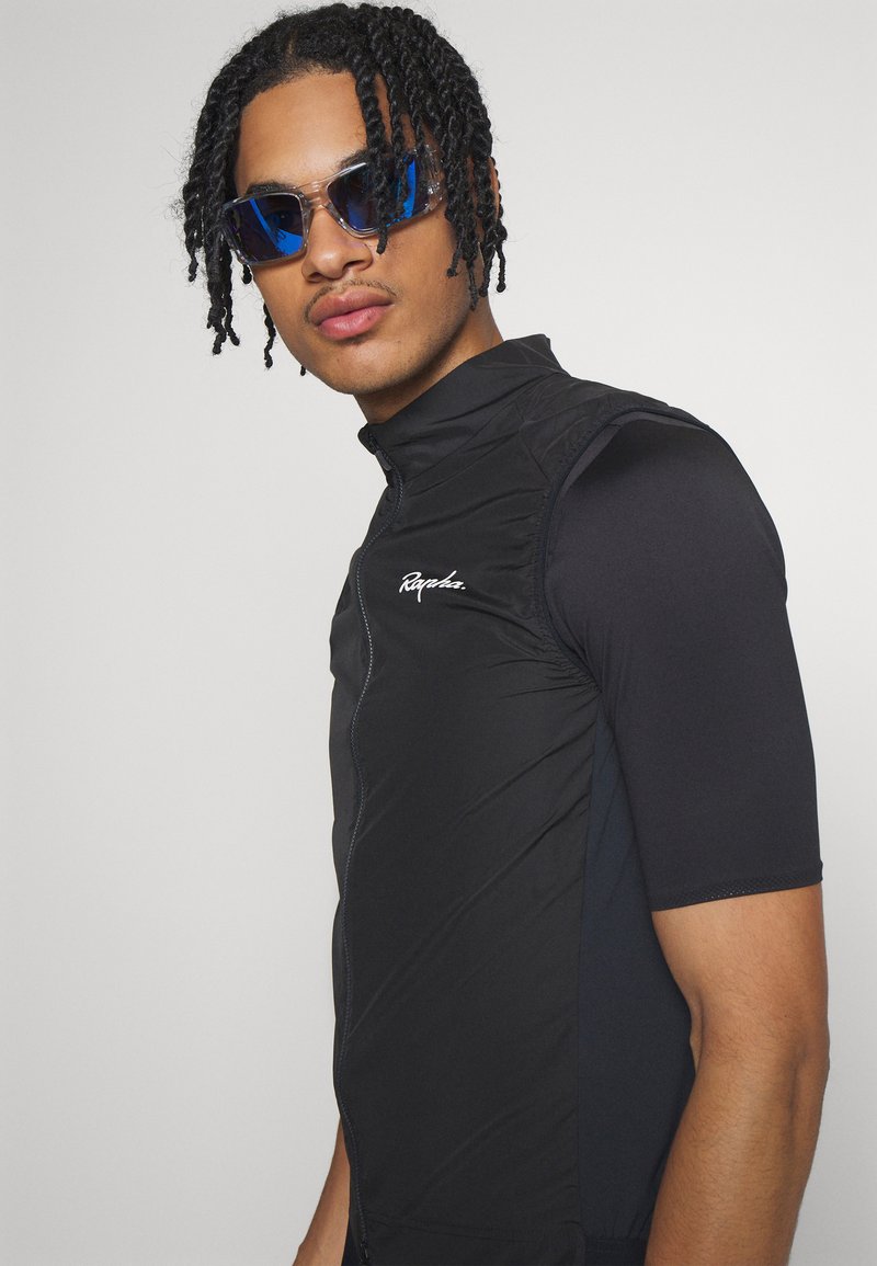 Gilet de vélo noir avec un col haut, des manches courtes et une fermeture éclair. Présente des coutures latérales discrètes et un logo blanc sur la poitrine. Accents réfléchissants.