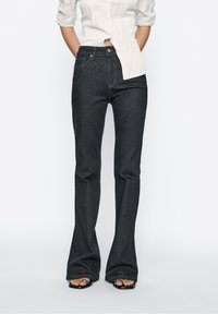 Dark denim flared jeans with a mid-rise waist, featuring subtle contrast stitching and a classic five-pocket design.