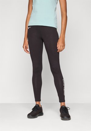 Sorte leggings med en tettsittende design, laget av elastisk materiale. Har hvit logo detalj på nederste del av benet. Kombinert med en lys blå topp og svarte sko.