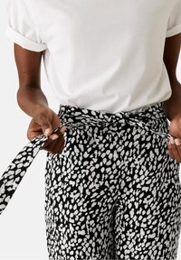 Schwarz-weiß gemusterte Hose mit einem gebundenen Bund. Der Stoff hat einen strukturierten, unregelmäßigen gepunkteten Druck mit einer glatten Baumwolloberfläche.