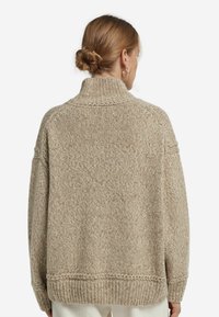 Beiger Strickpullover mit hohem Kragen und überschnittenen Schultern. Verfügt über ein strukturiertes Muster und einen gerippten Saum, was ihm ein gemütliches Aussehen verleiht.