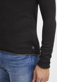 Svart langermet skjorte med ribbet tekstur, med en liten "BLEND" logo-merke ved kanten, sammen med blå denimjeans.