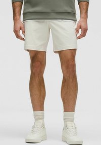 Witte sportshorts met een gladde textuur en een korte binnenbeenlengte, gecombineerd met witte hoge sneakers en geribbelde sokken.