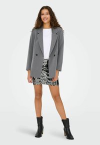 Pelēks divrindu žakets ar ieplestiem uzgaļiem, uzvilkts pār baltu kreklu un melnu mirdzošu mini svārku, kopā ar melnām potītēm līdzīgām kurpēm.