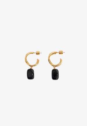 Boucles d'oreilles créoles en or avec des pendentifs en pierre noire rectangulaire irrégulière suspendus à chaque créole sur fond blanc.