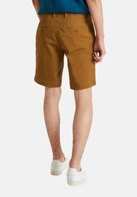 Shorts en coton marron avec une coupe droite, dotés de deux poches arrière et de passants de ceinture. Portés avec des baskets blanches.