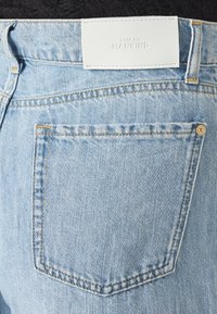 Jeans in denim blu chiaro con una tasca posteriore, cuciture gialle e un'etichetta in pelle bianca alla vita con la scritta "7 FOR ALL MANKIND."