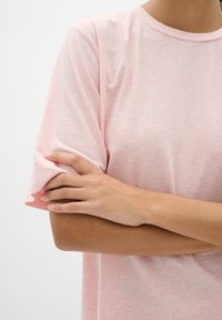 Šviesiai rožinė trumpomis rankovėmis marškinėliai su minkšta tekstūra, turintys apvalų kaklą ir subtilų margą raštą. Be siūlių rankovės ir laisvas siluetas.