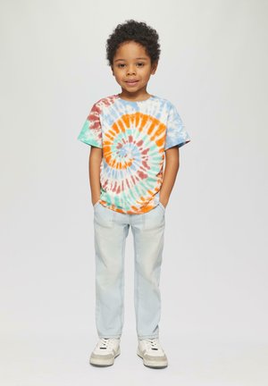 Farbiger Batik-T-Shirt mit einem Spiral-Muster in Orange, Blau und Türkis. Kombiniert mit hellblauen Jeans und weißen Sneakers.