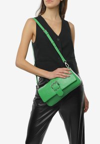 Grøn falsk læder crossbody taske med rektangulær form, der har en spænde-lukning og en justerbar strop. Teksturen er præget.