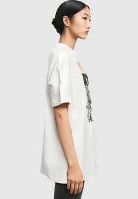 Hvid bomulds t-shirt med korte ærmer, prydet med et trykt grafisk design på forsiden. Løs pasform og rund hals.
