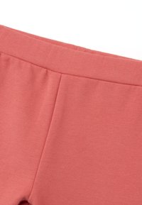 Cintura de tela elástica en color coral rosa con textura suave; presenta costuras sutiles y sin hardware visible, diseñado para un ajuste cómodo.