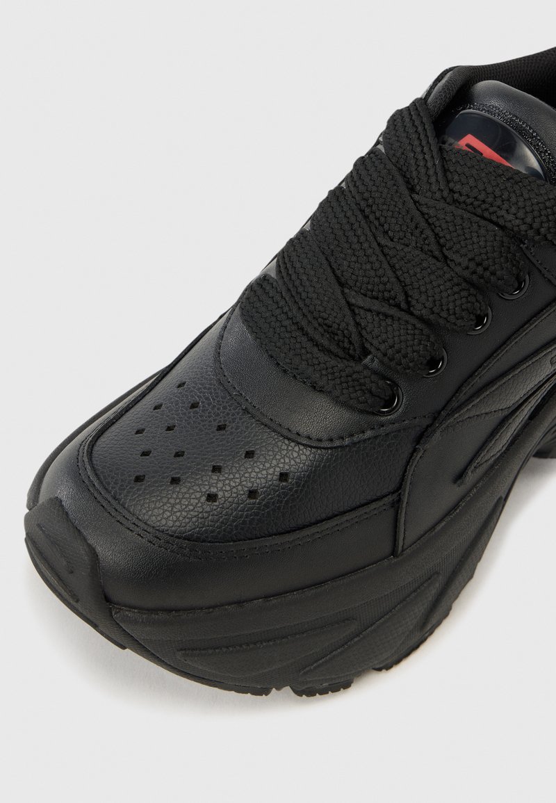 Baskets de sport noires en cuir lisse avec des accents texturés, présentant un design à lacets, des détails perforés et une semelle épaisse.