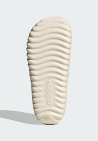 Adidaksin jalkineen pohja, beige, teksturoitu aaltoilevilla viivoilla, sisältää kuvatun logon, kumimateriaalia, jolla on sileä pinta.