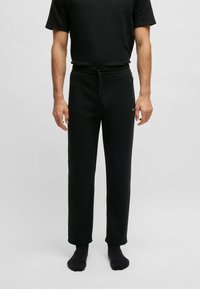 Zwarte katoenen sweatpants met een tailleband met koord, recht silhouet en subtiele textuur. Model draagt zwarte sokken.