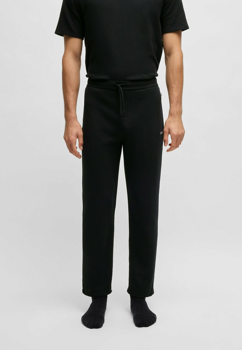 Zwarte katoenen sweatpants met een tailleband met koord, recht silhouet en subtiele textuur. Model draagt zwarte sokken.