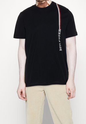 T-shirt noir à manches courtes en coton, avec une rayure verticale rouge et blanche et le logo "HILFIGER" sur le côté gauche.