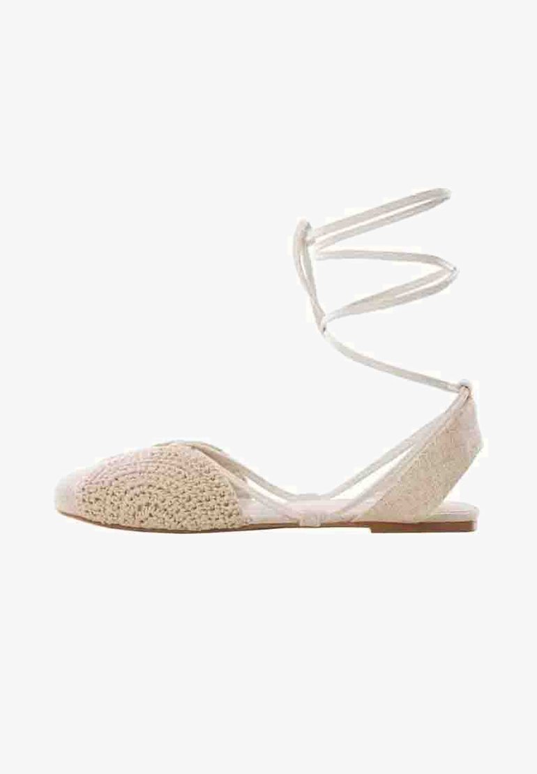 Beige tasapohjaiset kengät, joissa on tekstuurilla valmistettu virkkausosa edessä ja sileä takaosa. Ominaisuuksiin kuuluvat ohuet, ristikkäin menevät nilkkaremmit ja tasapohja.