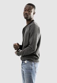Maglione grigio con scollo a V, maniche lunghe e polsi a coste, abbinato a jeans blu. Il maglione ha una texture liscia e un design aderente.