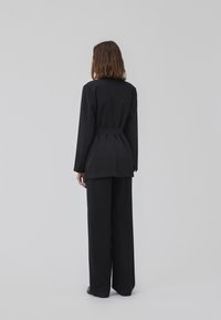 Sort skræddersyet jakkesæt med en blazer med bælte og vidde bukser. Glat stof, struktureret design og minimalistisk silhuet.