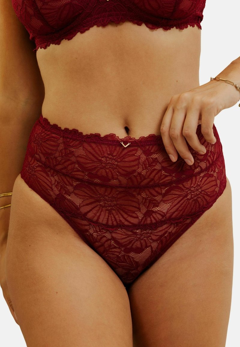 Culotte haute en dentelle rouge avec des motifs floraux et des bords festonnés, ornée d'un petit accent en forme de cœur à la taille.
