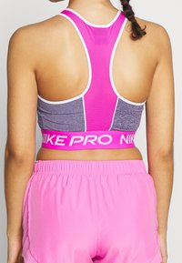 Brassière de sport grise et rose avec des détails en mesh et une large bande rose ornée d'un logo blanc ; associée à un short rose clair.