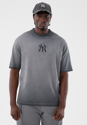 Uomo che indossa un berretto da baseball grigio, una T-shirt a gradiente grigio e pantaloni grigi, ciascuno con un logo NY nero intrecciato.