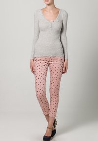 Gray ribbed long-sleeve top with a V-neck and three buttons, paired with pink dotted pants. Model wears dark shoes with a wedge heel.