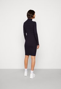 Vestito a coste navy con colletto alto e maniche lunghe, che si restringe fino al ginocchio; presenta strisce testurizzate nella parte superiore.