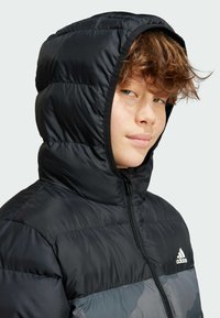 Veste à capuche noire rembourrée avec des accents gris, dotée d'une fermeture éclair et du logo Adidas. Texture lisse avec des sections matelassées.