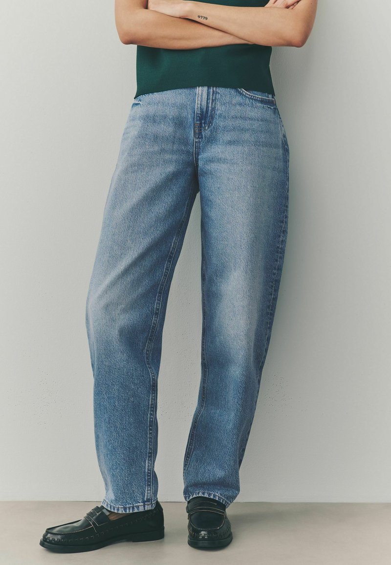Jeans de mezclilla azul claro con un corte relajado, piernas rectas y una textura ligeramente desgastada. Usados con mocasines negros.