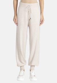 Jasno beżowe dresy z polaru z elastycznym paskiem, zwężanymi mankietami i bocznymi kieszeniami, w zestawie z białymi trampkami.