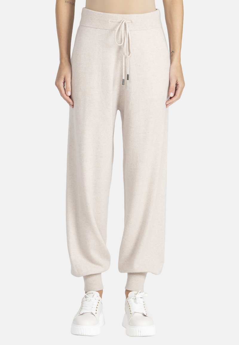 Jasno beżowe dresy z polaru z elastycznym paskiem, zwężanymi mankietami i bocznymi kieszeniami, w zestawie z białymi trampkami.