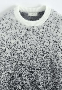 Pull en tricot avec un motif dégradé allant du blanc au gris, texture douce, encolure ronde et poignets côtelés. Étiquette de marque visible.