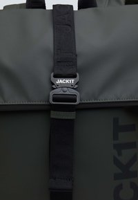 Grå vattentät ryggsäck med ett svart justerbart rem med spänne. Texturerat material med en jämn yta och logodetalj.