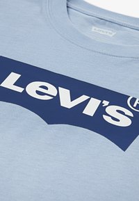 Lyseblå t-skjorte med stor mørkeblå Levi's-logo med hvit tekst. Korte ermer og rund hals med en jevn tekstur.