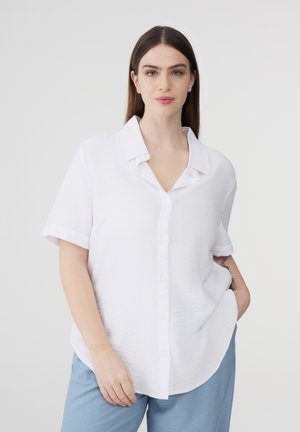 Camicetta bianca a maniche corte con colletto, realizzata in un tessuto strutturato e con una vestibilità rilassata, abbinata a pantaloni azzurri chiari.