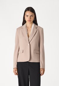 Blazer in light beige fabric with a lapel collar, single button closure, and two front pockets; tailored fit, minimal seams, and smooth texture.