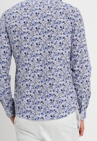 Camicia a maniche lunghe con un motivo floreale blu e bianco, dotata di colletto button-down e tessuto liscio, progettata con una silhouette aderente.